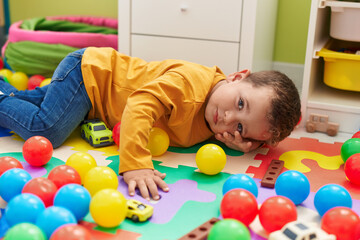 Adorable caucasian boy playing with balls lying on floor at kindergarten