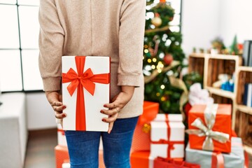 Hispanic brunette woman hiding christmas present at home