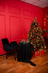 Red Christmas background with a decorated Christmas tree, an armchair, a table with candles and a fireplace.