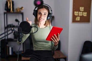 Hispanic woman singing song using microphone and tablet smiling happy and positive, thumb up doing excellent and approval sign