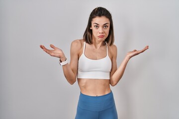 Fototapeta na wymiar Hispanic woman wearing sportswear over isolated background clueless and confused expression with arms and hands raised. doubt concept.