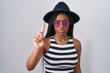Young african american with braids wearing hat and sunglasses pointing with finger up and angry expression, showing no gesture