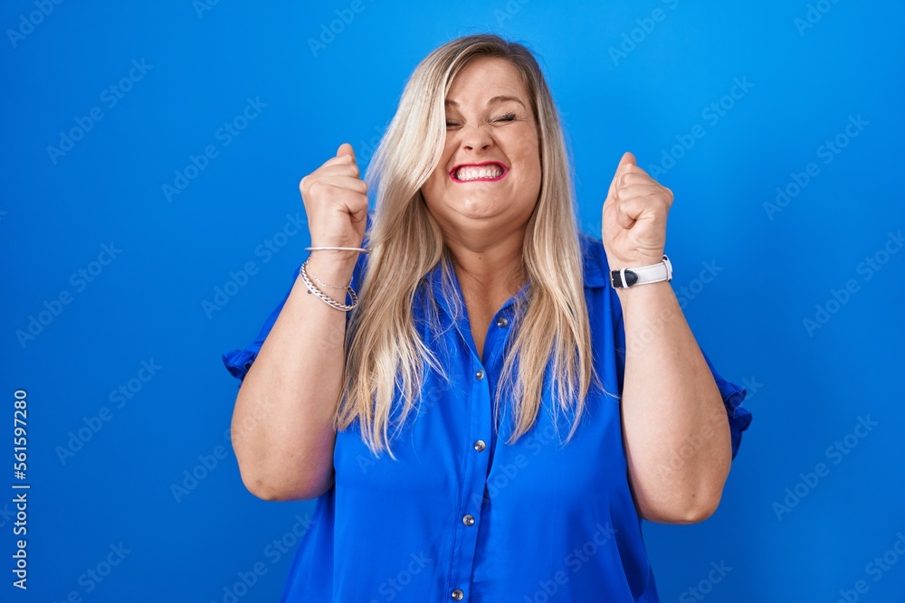 Sticker Caucasian plus size woman standing over blue background excited for success with arms raised and eyes closed celebrating victory smiling. winner concept.