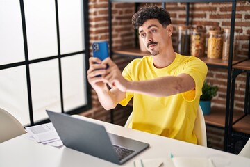 Hispanic man doing video call with smartphone looking positive and happy standing and smiling with a confident smile showing teeth