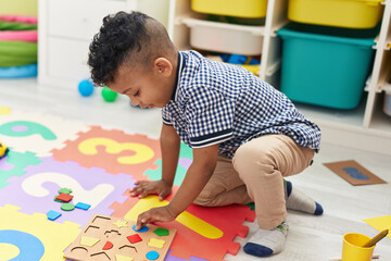 African american boy playing with maths puzzle game sitting on floor at kindergarten