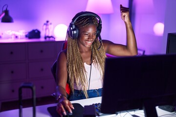 African american woman streamer playing video game with winner expression at gaming room