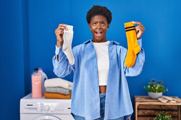 African american woman holding clean andy dirty socks angry and mad screaming frustrated and...