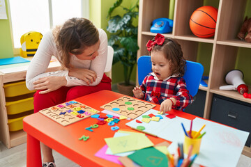 Fototapeta premium Teacher and toddler playing with maths puzzle game sitting on table at kindergarten