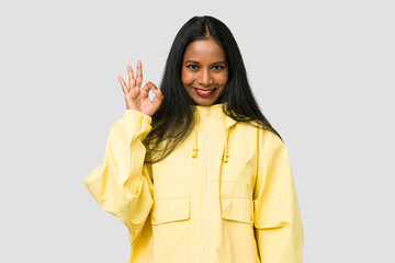 Young Indian woman cut out isolated on white background winks an eye and holds an okay gesture with hand.