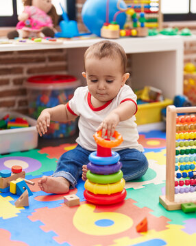 Adorable hispanic baby playing with abacus and hoops game sitting on floor at kindergarten