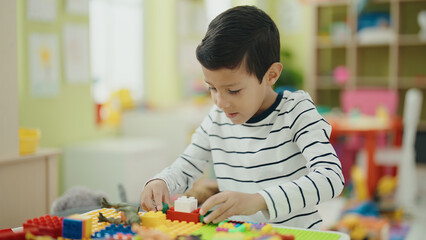 Adorable hispanic boy playing with construction blocks sitting on table at kindergarten