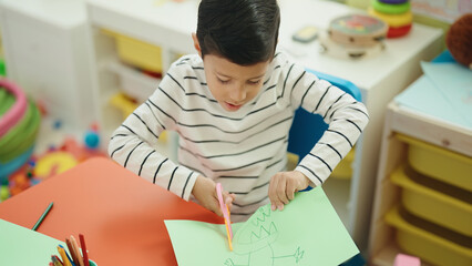 Adorable hispanic boy student cutting paper at kindergarten