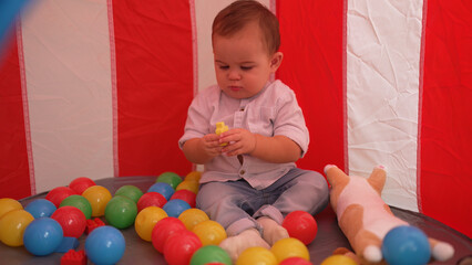 Fototapeta na wymiar Adorable toddler playing with toys sitting inside of circus tent at home