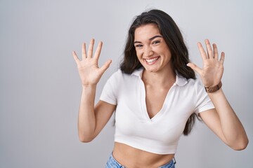 Young teenager girl standing over white background showing and pointing up with fingers number ten while smiling confident and happy.