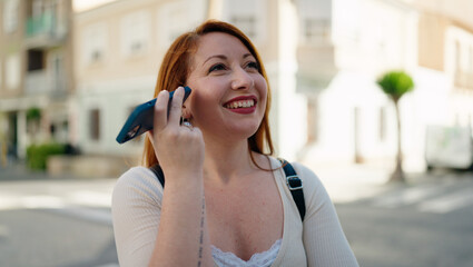 Young redhead woman smiling confident listening audio message by the smartphone at street