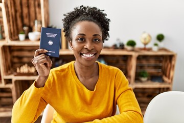 African american woman holding deutchland passport sitting on table at home