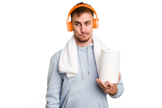 Young fitness man listening to music and holding a protein bottle isolated cut out confused, feels doubtful and unsure.