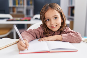 Adorable hispanic girl student sitting on table doing homework at classroom