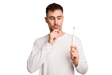 Young caucasian man holding an electric toothbrush isolated cut out looking sideways with doubtful and skeptical expression.