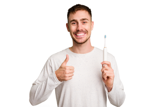 Young caucasian man holding an electric toothbrush isolated cut out smiling and raising thumb up