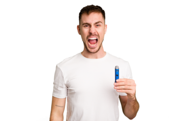 Young caucasian man holding a vaporizer cut out isolated screaming very angry and aggressive.