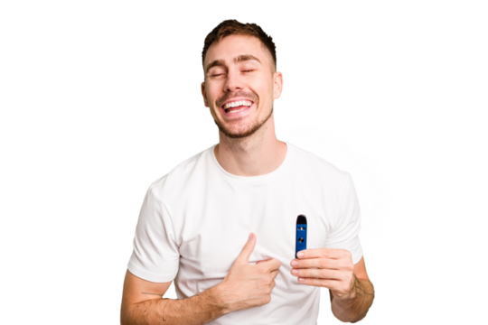 Young caucasian man holding a vaporizer cut out isolated laughing and having fun.