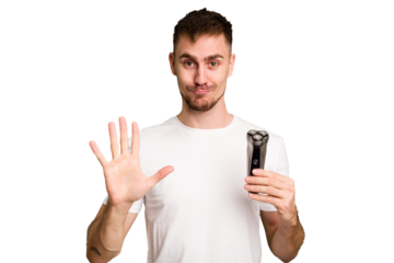 Young man holding a shaving machine cut out isolated smiling cheerful showing number five with fingers.