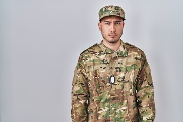 Young hispanic man wearing camouflage army uniform skeptic and nervous, frowning upset because of...