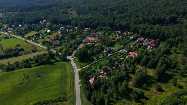 Mountain village and road with moving cars, aerial view. Beautiful mountain landscape with residential neighborhood and green fields. Countryside view