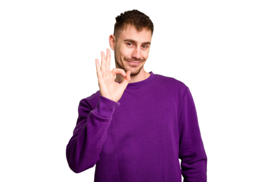 Young caucasian man cut out isolated winks an eye and holds an okay gesture with hand.