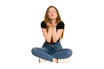 Young redhead woman sitting on the floor cut out isolated folding lips and holding palms to send air kiss.