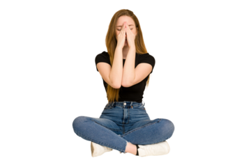 Young redhead woman sitting on the floor cut out isolated holding hands in pray near mouth, feels confident.