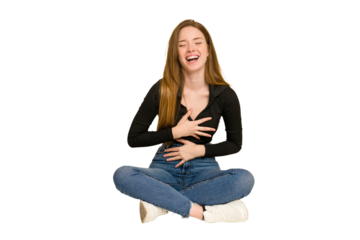 Young redhead woman sitting on the floor cut out isolated laughing and having fun.