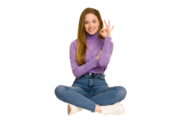 Young redhead woman sitting on the floor cut out isolated raising both thumbs up, smiling and confident.