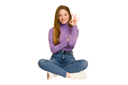 Young redhead woman sitting on the floor cut out isolated raising both thumbs up, smiling and confident.