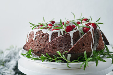 Christmas chocolate bundt cake. Traditional Christmas fruit cake with white glaze, cranberries and rosemary on white stand with Christmas decoration. Winter baking at Xmas or New Year. Copy space.