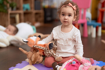 Adorable caucasian girl playing with doll sitting on floor at kindergarten