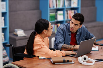 Fototapeta premium Teenage girl in wheelchair studying with friend in college library