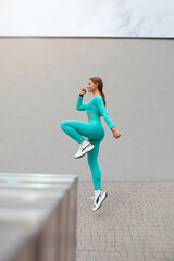 Young sportive woman, woman with beautiful body, jumping and running on gray background, female model in sportswear exercising outdoors