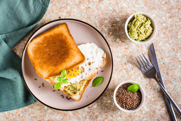 Sandwich with avocado, fried egg and flax seeds on toast on a plate on the table. Top view
