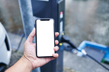 Man holding smartphone showing white blank screen at electrical car station