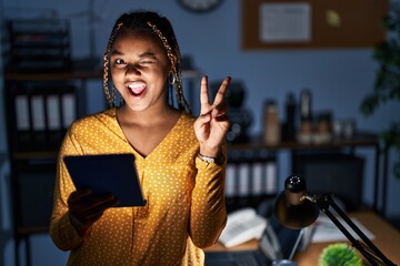 African american woman with braids working at the office at night with tablet smiling with happy...
