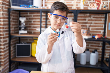 Adorable hispanic boy student looking molecules at laboratory classroom