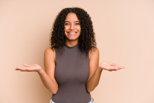 Young african american curly woman isolated makes scale with arms, feels happy and confident.