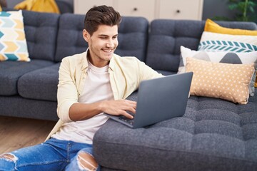 Young hispanic man using laptop sitting on floor at home