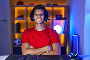 Young hispanic man playing video games happy face smiling with crossed arms looking at the camera. positive person.