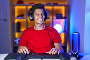 Young hispanic man playing video games looking away to side with smile on face, natural expression....