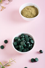 Obraz na płótnie Canvas Detox and antioxidant. Matcha powder and spirulina pills in bowls on a pink. Vertical view