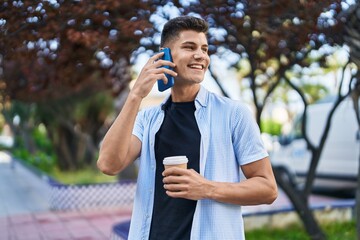 Young hispanic man talking on the smartphone drinking coffee at park