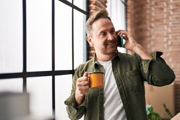 Young caucasian man talking on smartphone drinking coffee at new home